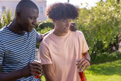 Diverse young male friends sharing drinks and laughing in sunny backyard garden