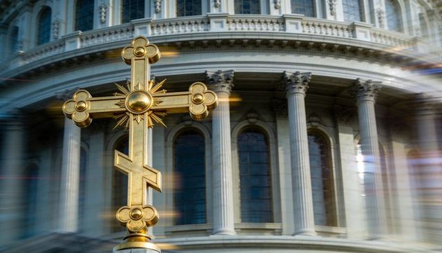 Gilded orthodox cross gleaming against neoclassical cathedral dome with sunlit flare, detail