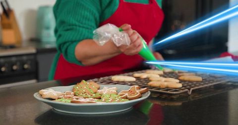 Home baker decorating gingerbread cookies with green icing and holiday sprinkles