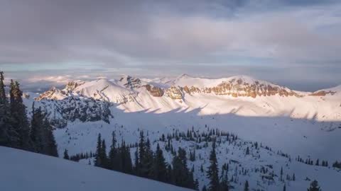 Panning aerial reveal of snow-covered alpine ridge and basin with conifers at golden hour