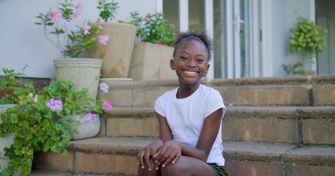 Smiling young girl sitting on sunlit stone steps with pink planters for family lifestyle