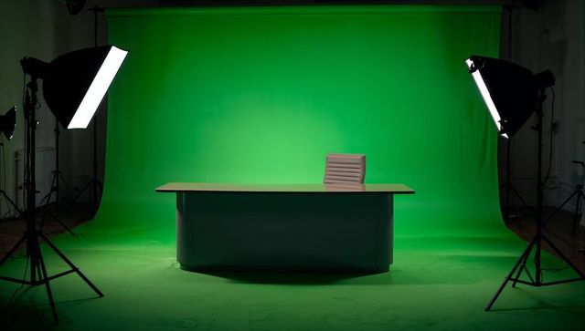 Desk and swivel chair on green chroma-key backdrop with softbox studio lighting