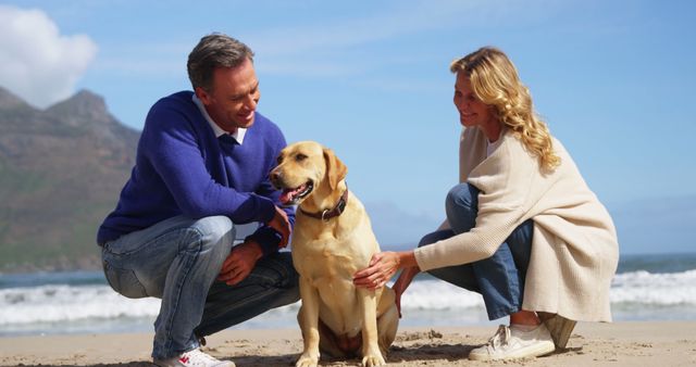 Man and woman crouching on sandy beach, smiling at each other while petting their dog. The scene depicts leisure, bonding with pets, and enjoying nature. Ideal for advertisements related to travel, vacations, pet care, and lifestyle content.