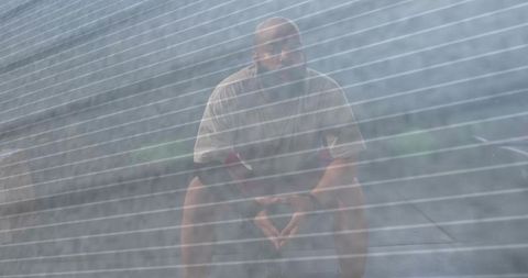 Man pausing on bench seen through striped mesh conveying urban solitude and contemplation