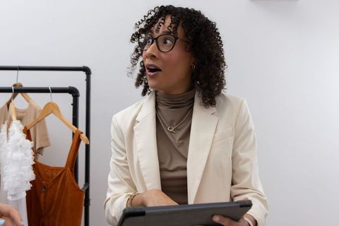 African american boutique stylist advising customer holding tablet and smiling in boutique