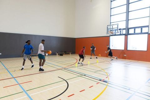 Diverse male basketball players practicing dribbling, defense and teamwork on indoor court