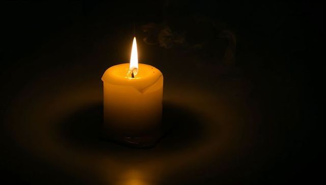 Glowing pillar candle casting warm circular halo on dark reflective surface