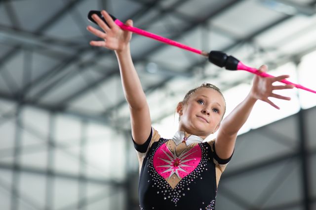 Caucasian female gymnast practicing at the gym, using a stick to and twisting it in her hands. Gymnast training hard for competition.