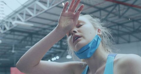 Exhausted athlete wiping brow after intense workout, wearing face mask in industrial gym