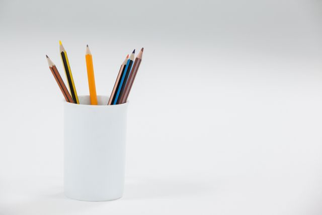 Colored pencils in a white cup on a white background. Ideal for use in educational materials, office supply advertisements, art and craft promotions, and minimalist design projects. The clean and simple composition emphasizes the tools and can be used to convey themes of creativity, organization, and simplicity.