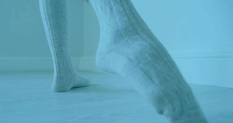 Woman lifting feet in thick knit socks on pale wooden floor