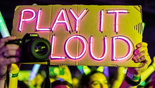 Neon play it loud cardboard sign held above cheering crowd, dslr camera and glowsticks