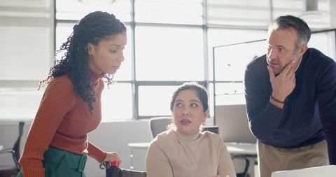 Diverse team collaborating at laptop in modern sunlit open-plan office