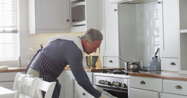 Happy caucasian man wearing apron, standing in kitchen, cooking dinner - Download Free Stock Photos Pikwizard.com
