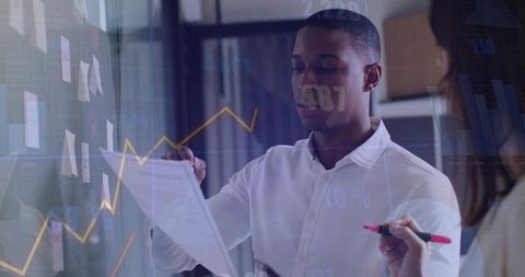 Business team presenting data on glass wall with sticky notes and financial charts for strategy