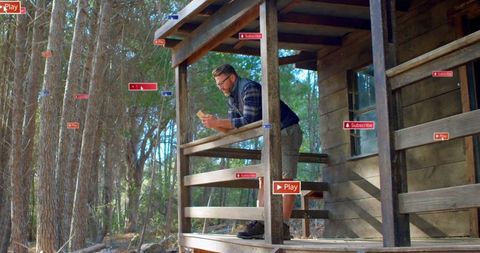 Man Engaging with Smartphone on Cabin Porch in Wilderness