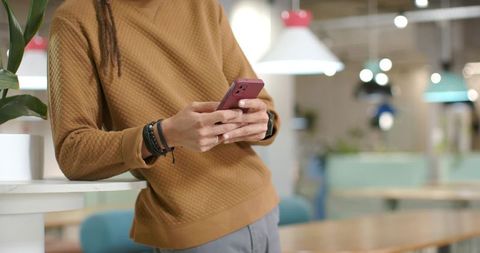African Man Leaning on Counter Texting on Pink Smartphone in Modern Coworking Space
