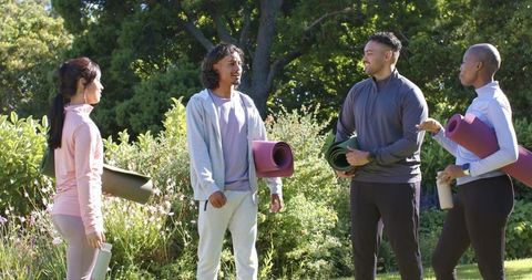 African american friends meeting for outdoor yoga holding mats and bottles in sunlit park