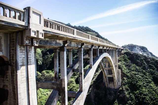 Historic arched concrete bridge stretching over a deep green canyon, showcasing impressive architectural design. Ideal for use in travel guides, engineering presentations, tourism campaigns, and scenic landscape projects.