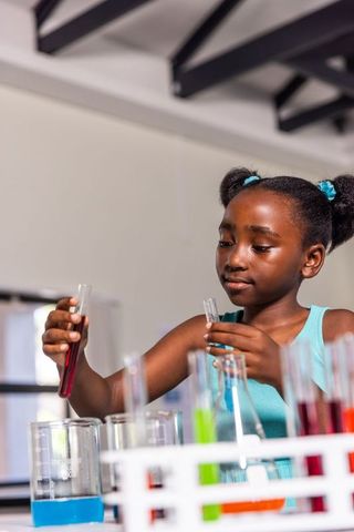 African american girl conducting colorful chemistry experiment with test tubes in school lab