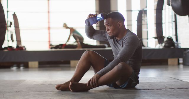 Image of fit and tired african american man resting after training at gym. active, fit, sporty and healthy lifestyle, exercising at gym concept.