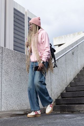 African american commuter descending urban steps wearing pink hoodie, beanie, backpack