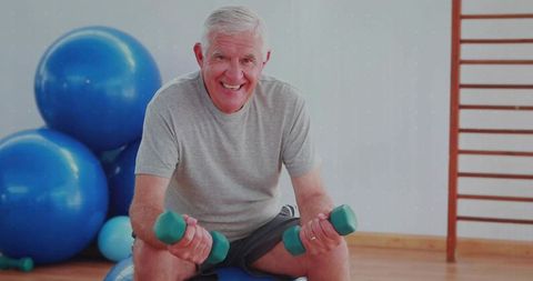 Senior Man Exercising with Dumbbells on Stability Ball in Fitness Studio