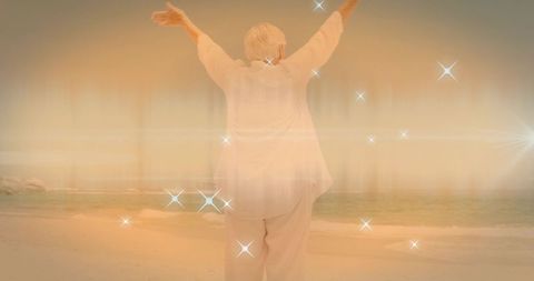 Senior woman raising arms toward ocean on glowing beach at golden hour