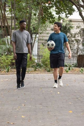 Young african american men walking and talking in park holding soccer ball casual sportswear