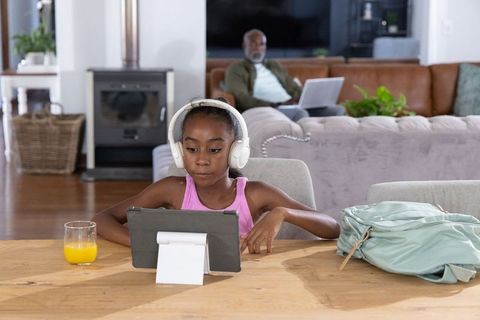 African girl using tablet with headphones at home while older man working on laptop