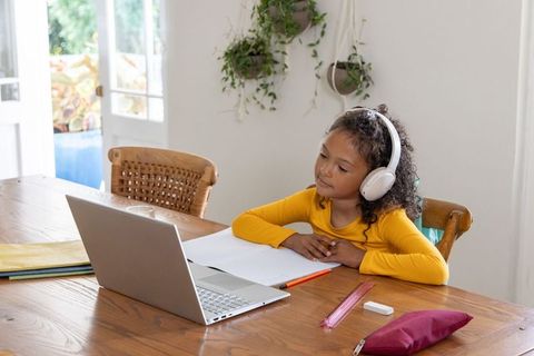 African american girl studying at home using laptop and headphones at dining table