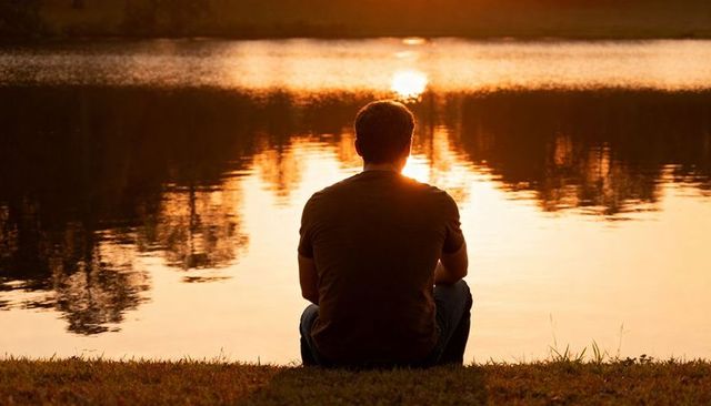 Man sitting at lakeside during sunset reflecting on solitude and golden hour calm