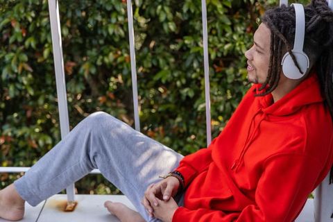 African american man relaxing on balcony listening to music in red hoodie