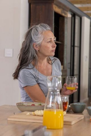 Contemplative senior woman sipping orange juice at cozy kitchen island