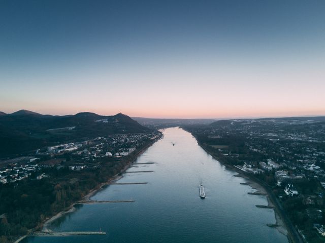 Capturing a picturesque aerial view of a river flowing through a valley flanked by towns and hills during sunset. Ideal for travel blogs, nature-themed articles, and transportation industry publications.