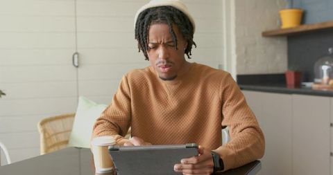 Young African American man concentrating on tablet with coffee in cozy minimalist kitchen