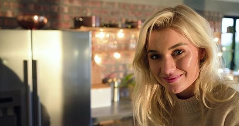 Smiling blonde woman standing in warm modern rustic kitchen with stainless refrigerator