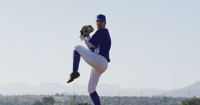 Baseball player in full pitcher's uniform captured mid-pitch against a clear blue sky on a sunny day. Useful for demonstrating athleticism, sports training materials, outdoor activities promotion, competitive sports imagery, or team portraits.