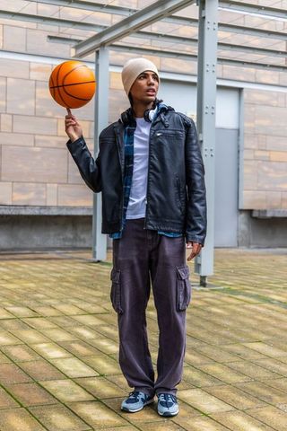 Urban young man balancing basketball on fingertip wearing leather jacket and beanie
