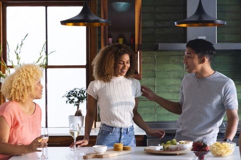Multiracial friends chatting around kitchen island with wine glasses and snack board