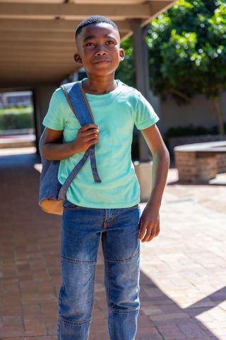 African american boy standing on school campus holding backpack, thoughtful expression
