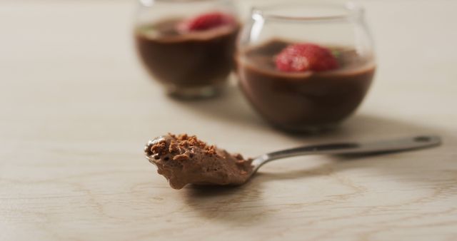 Close-up of creamy chocolate mousse on a spoon with two glasses of chocolate mousse and strawberries in the background. Ideal for food blogs, dessert recipes, and culinary websites. Emphasizes indulgence and gourmet dessert presentation.