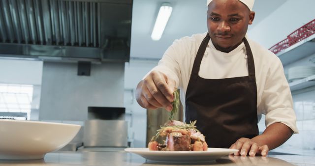 Chef wearing uniform competently adds fresh herbs to a carefully prepared dish, demonstrating advanced culinary skills. This can be used for restaurant advertisements, culinary school promotions, food blogs, and articles on professional cooking and restaurant management.