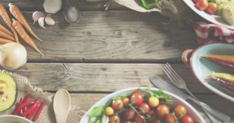Rustic wooden tabletop featuring cherry tomatoes, heirloom carrots, garlic and kitchen utensils