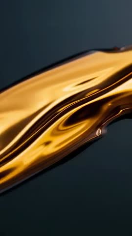 Vertical video of golden liquid ribbon sliding across dark surface forming glossy beads