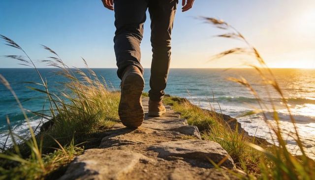 Man walking cliffside trail at sunset with hiking boots and ocean view