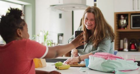 Mother and Daughter Smiling in Kitchen with Smartphone