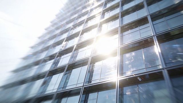 Sunlit glass facade of modern high-rise with grid mullions, lens flare, urban corporate