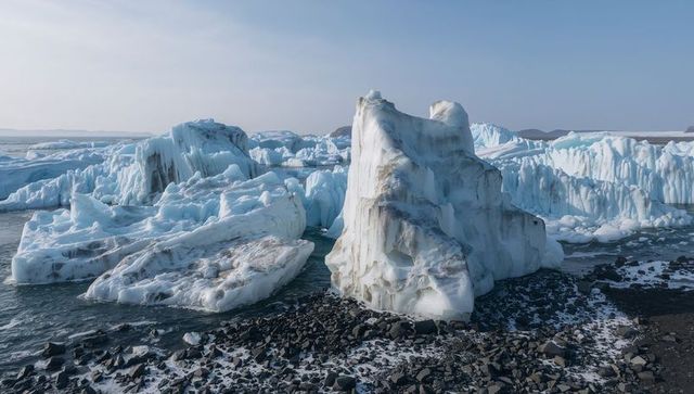Towering iceberg resting on rocky arctic shore with sediment streaks and broken floes