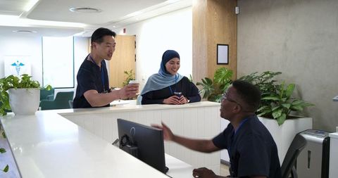 Multicultural healthcare team at modern clinic reception handing coffee, smiling